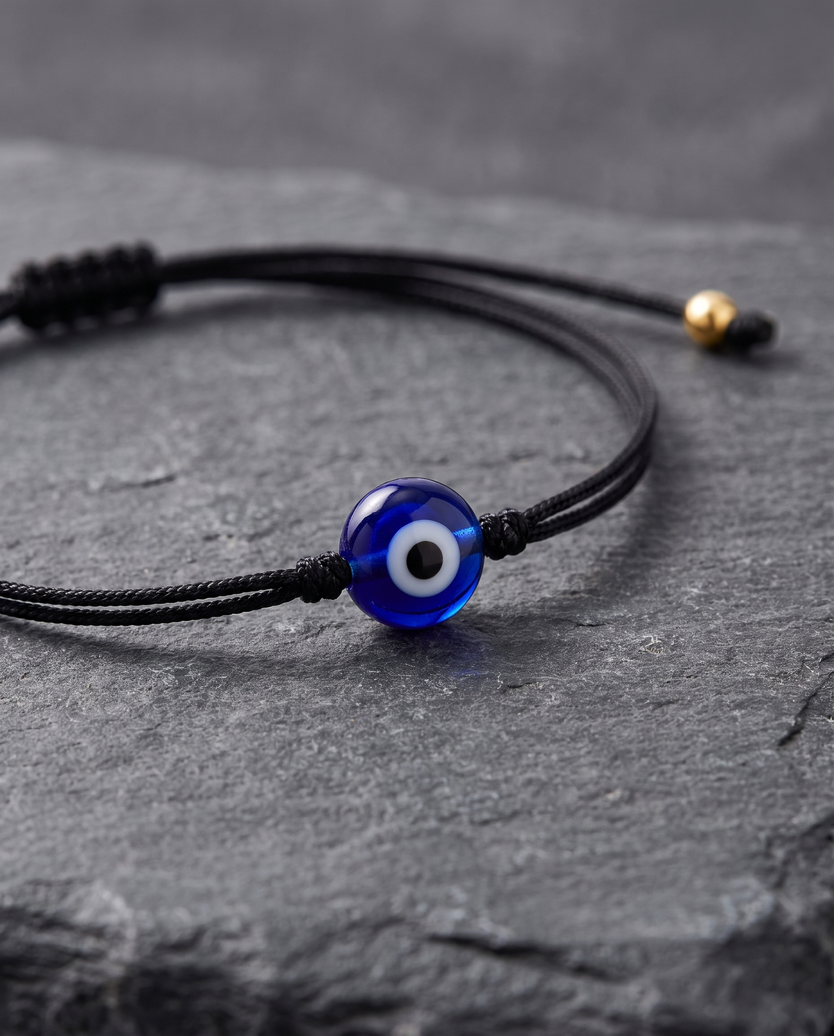 Close-up of the Greek Eye Cord bracelet: thin black Italian Supima cord with a blue glass evil-eye charm and gold tips