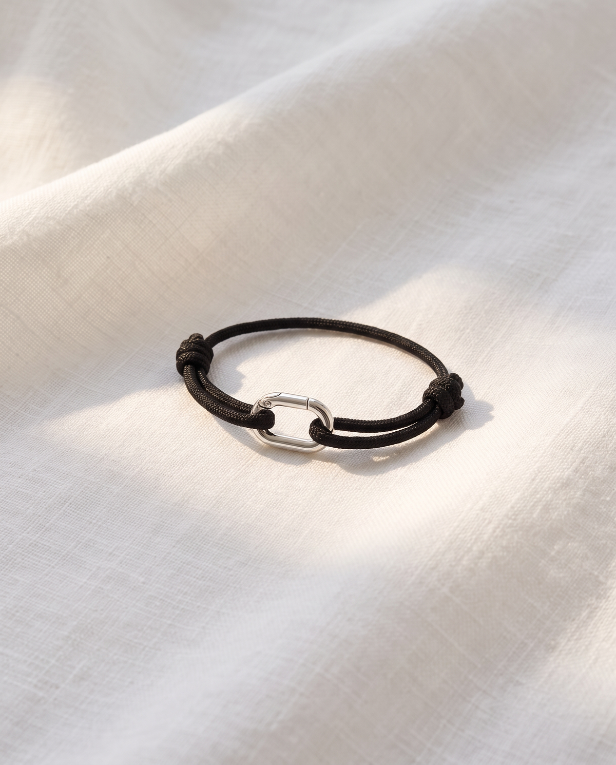 Verona Silver cord bracelet with silver oval link resting on white linen fabric