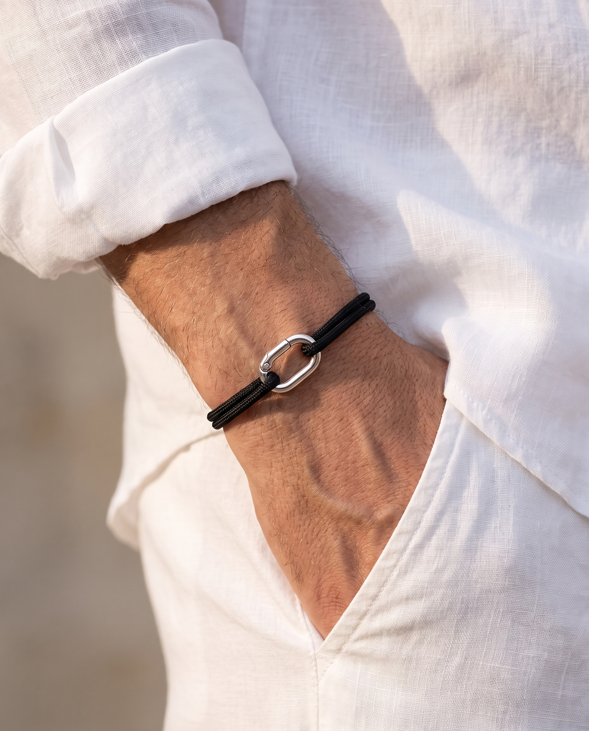 Man in a white linen shirt wearing the Verona Silver cord bracelet, hand in his white linen trouser pocket