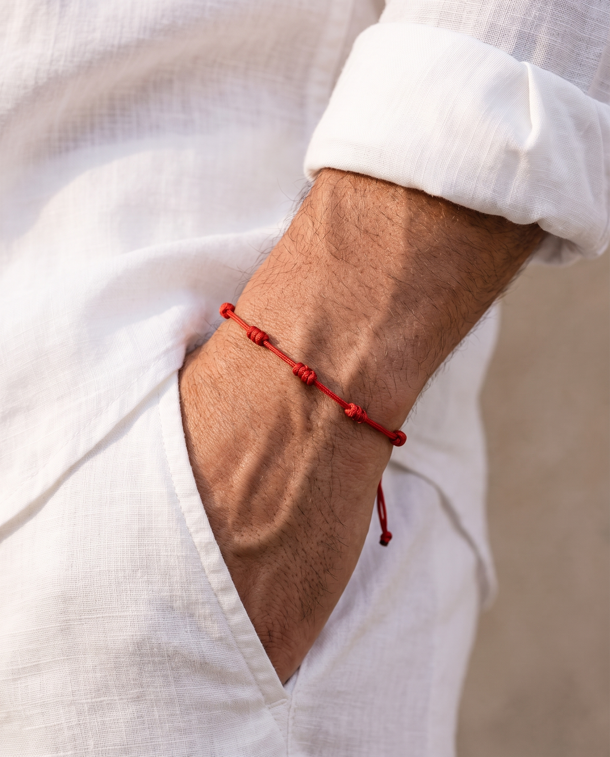 Man in a white linen shirt wearing the Barletta Knot red knotted cord bracelet, hand in his white linen trouser pocket