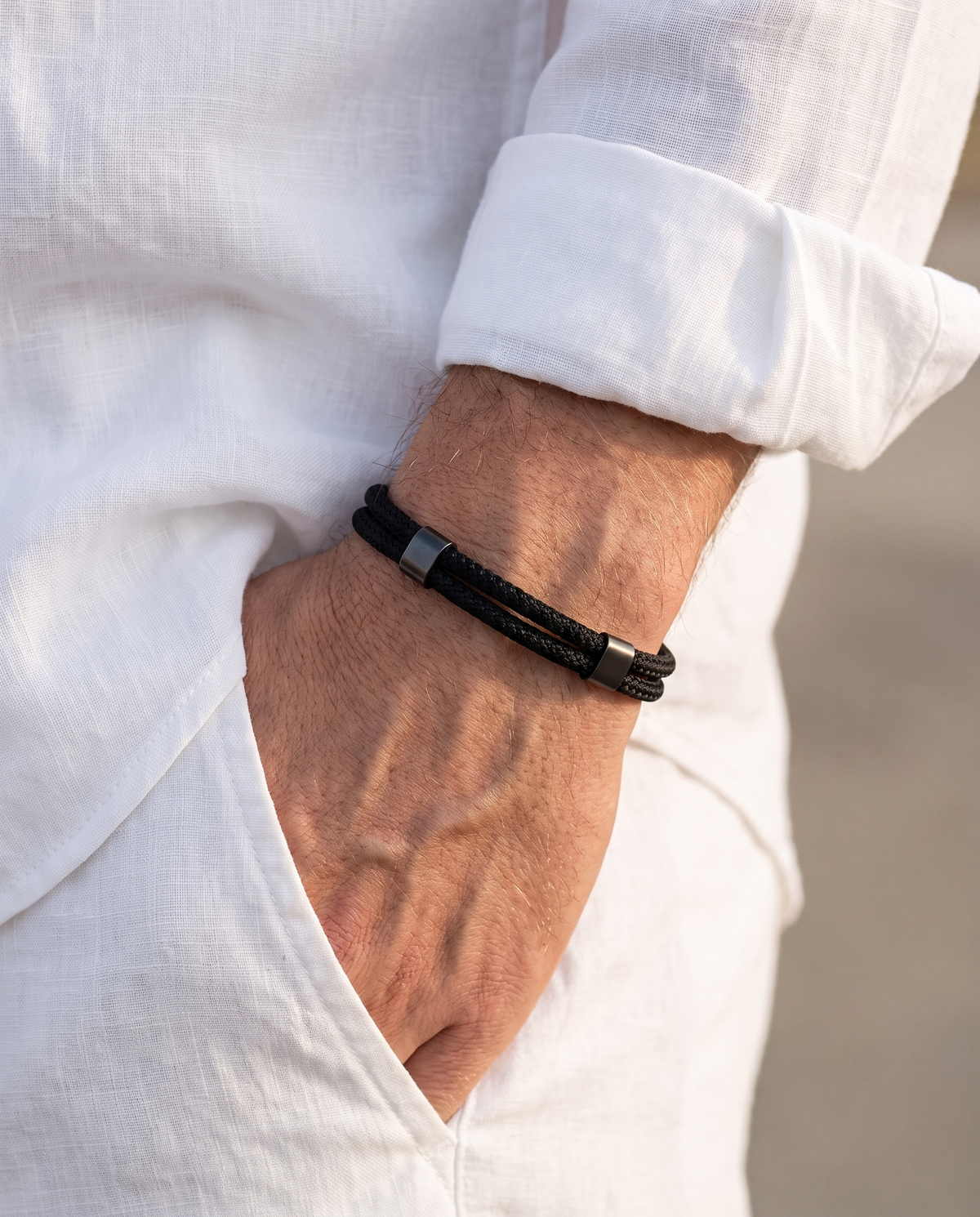 Man in a white linen shirt wearing the Porto Nautical Cord braided rope bracelet, hand in his white linen trouser pocket