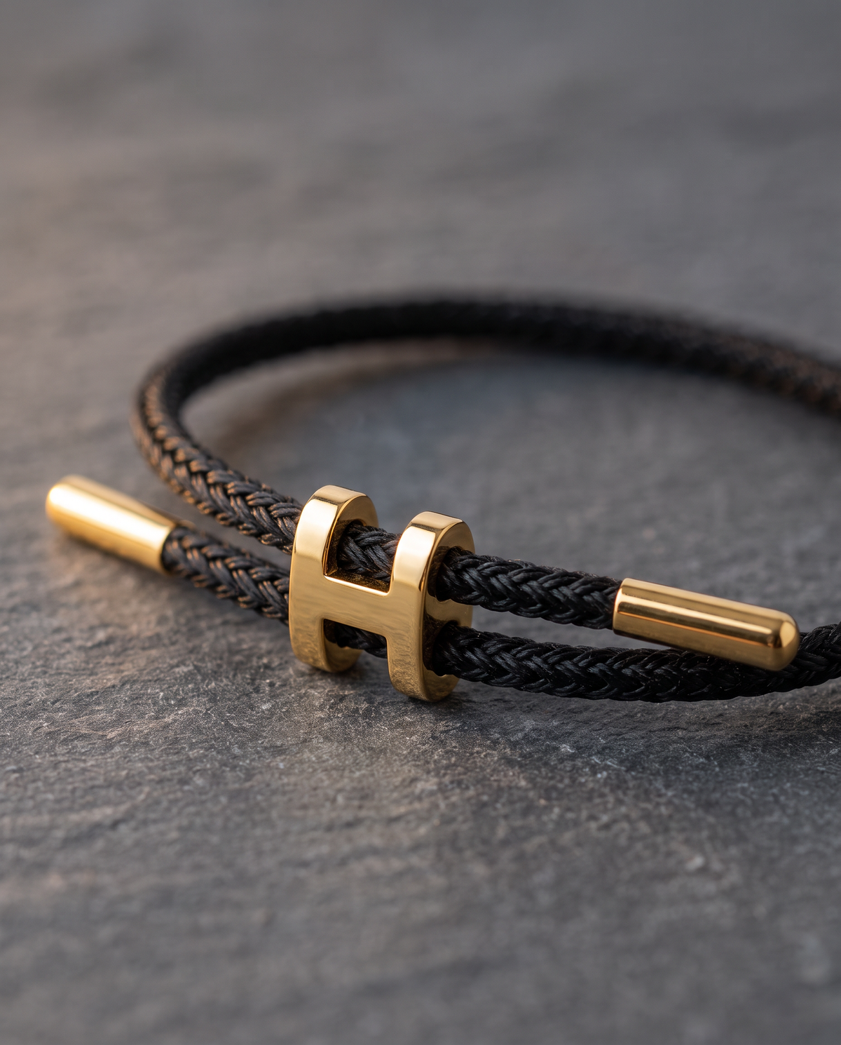 Close-up of the Hills Braid black braided Supima cord bracelet with polished 18k gold-plated H centerpiece