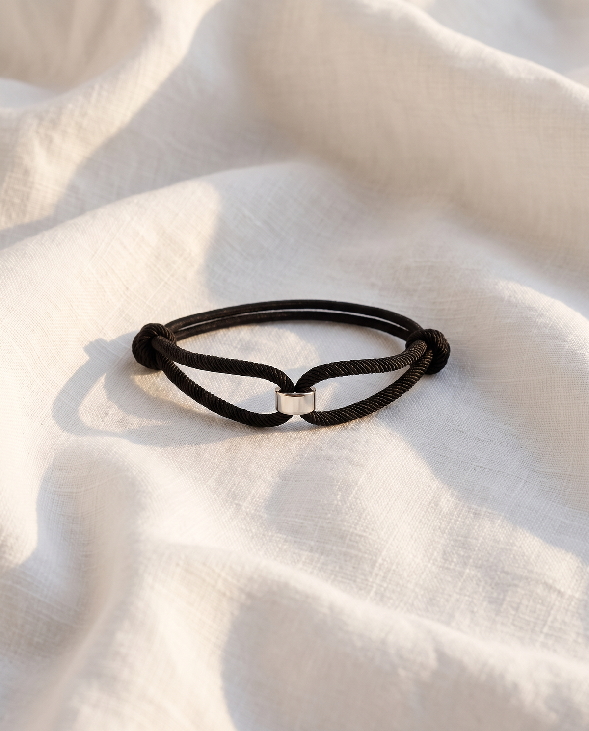Milan Cord bracelet with silver barrel centrepiece resting on white linen fabric